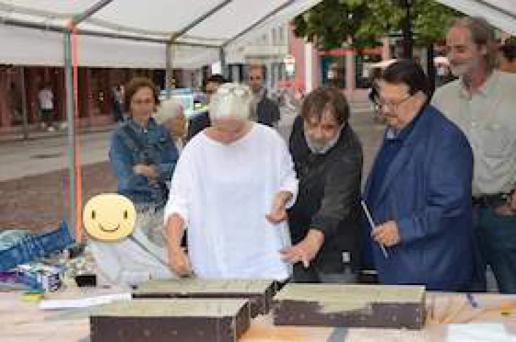 Wem gehört Heimat? Kunstaktion auf dem Universitätsplatz in Heidelberg. Teilnehmer*innen ritzen die Worte MIT WÜRDE LEBEN in Mörtel.